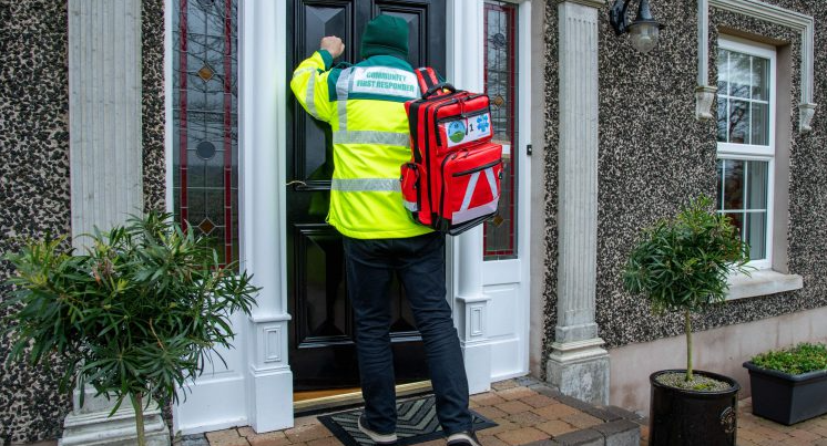 A NIAS community first responder carrying a red medical backpack knocking on a house front door