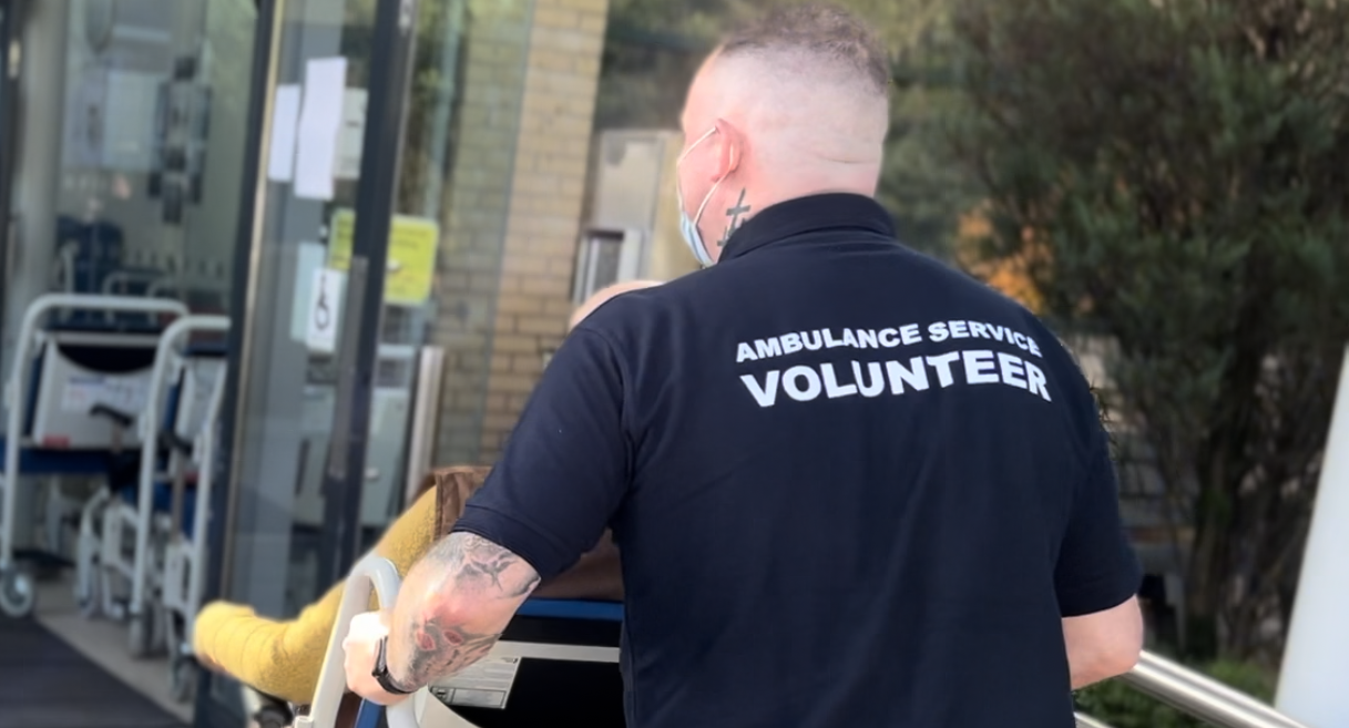 An ambulance service volunteer pushing a patient in a wheelchair into a medical facility