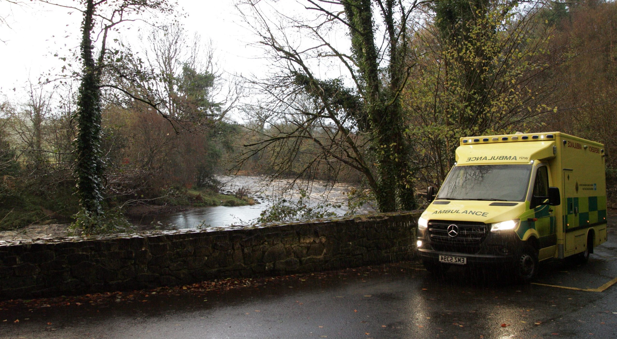 An ambulance parked beside a wall overlooking a river and trees