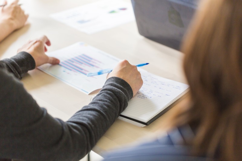 Photo of a person sitting at a meeting room desk making notes and viewing a report